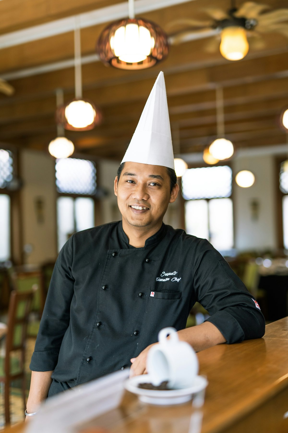 A smiling chef in a black chef's jacket in a restaurant dining room
