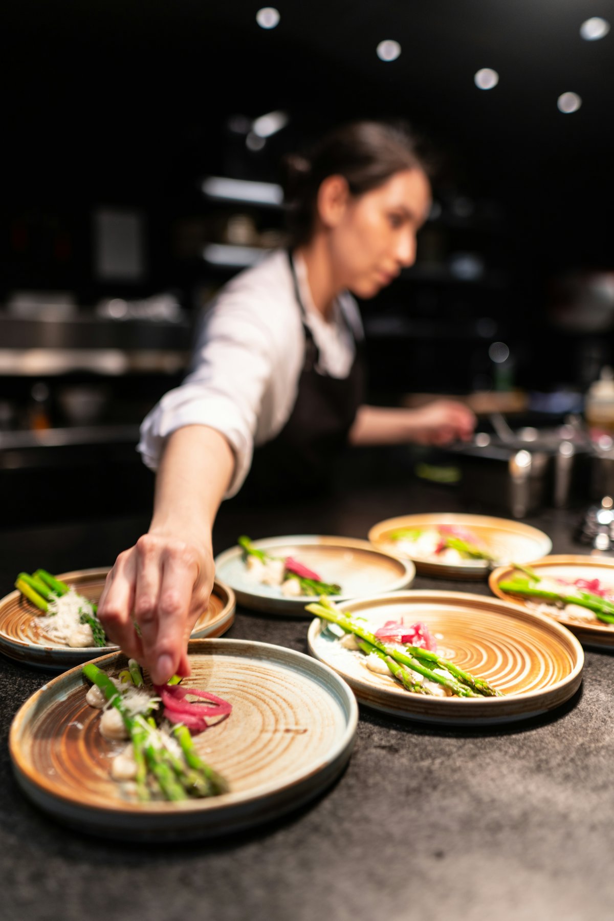 A female chef plating dishes at the pass in a dark professional kitchen