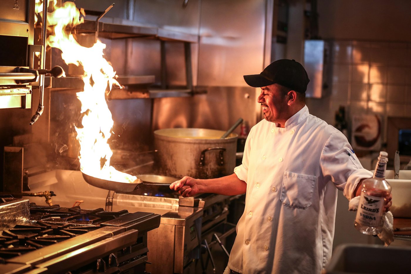 A chef working over a flaming pan on a busy range