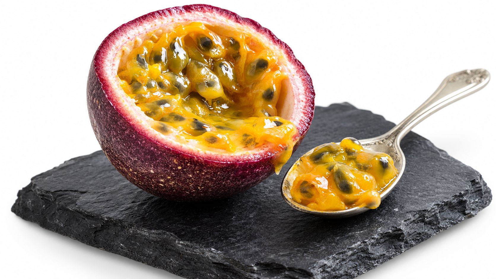 A halved purple passion fruit with bright yellow pulp and black seeds served on a black stone plate.